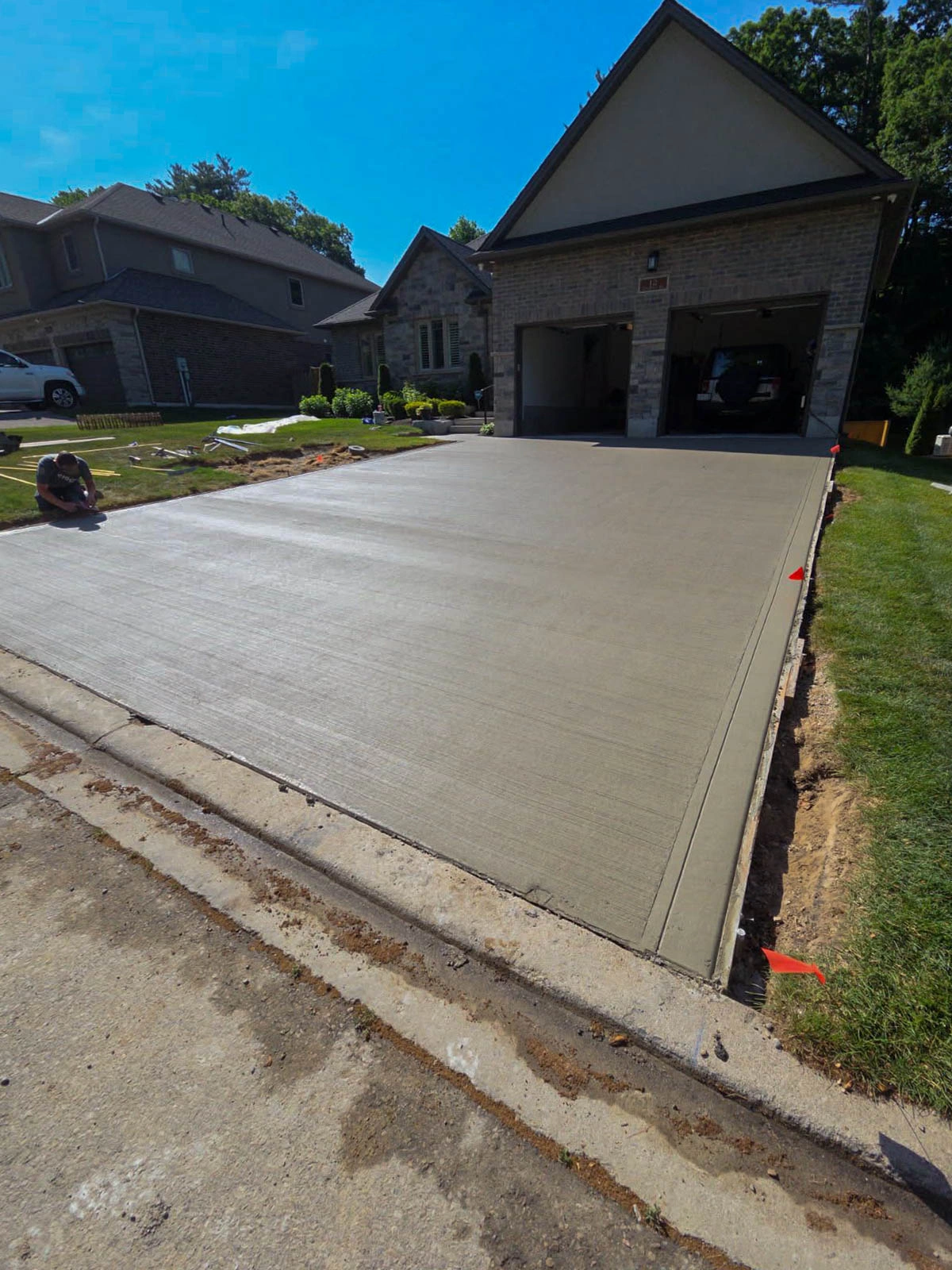 A newly poured concrete driveway in front of a house, with safety markers on the edges and a person sitting on the left side.