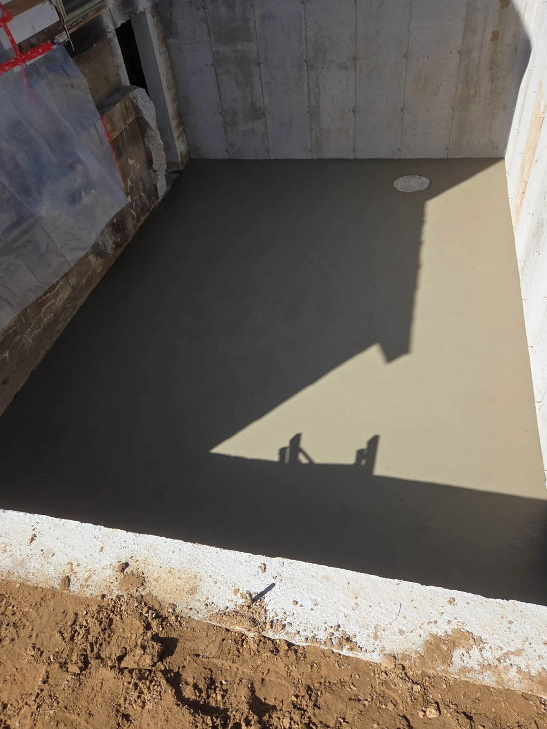 Freshly poured concrete slab inside a partially constructed room with a floor drain visible near the wall.